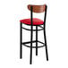 A bar stool with a black metal frame, red vinyl seat, and an antique walnut wood backrest.
