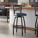 A black metal swivel bar stool with a cross back design and a navy vinyl padded seat.