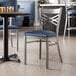 A metal cross back chair with a clear coat finish and a navy blue vinyl padded seat.