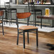 A black metal chair with a light brown vinyl seat and an antique walnut wood backrest.