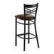 A black metal bar stool with a cross back design and a dark brown vinyl padded seat.