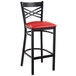 A Lancaster Table & Seating black cross back bar stool with a red padded seat.