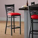 A Lancaster Table & Seating black cross back bar stool with a red vinyl padded seat.