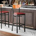 A bar stool with a black metal frame, burgundy vinyl seat, and cherry wood backrest.