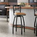 A black metal bar stool with a cross back design and a light brown vinyl padded swivel seat.