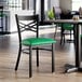 A black metal cross back chair with a green vinyl padded seat.