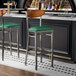 Two Lancaster Table & Seating bar stools with green vinyl seats and wood backs at a black bar counter.