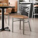 A metal cross back chair with a clear coat finish and a light brown vinyl padded seat.
