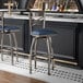 A metal bar stool with a cross back design and a navy blue vinyl padded seat.