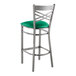 A Lancaster Table & Seating clear coated metal cross back bar stool with a green vinyl padded seat.