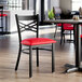 A black metal cross back chair with a red vinyl padded seat.