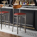 Two Lancaster Table & Seating bar stools with red vinyl seats at a black bar counter.