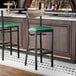 A bar stool with a black metal frame, green vinyl seat, and a driftwood-finished wooden backrest.