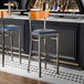 Two Lancaster Table & Seating Boomerang bar stools with navy seats and cherry wood backs at a black counter.