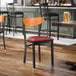 A black metal chair with a burgundy vinyl seat and a cherry wood backrest.