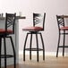 A close up of a black Lancaster Table & Seating swivel bar stool with a burgundy cushion.