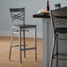 A Lancaster Table & Seating black wood cross back bar stool with a metal frame next to a table.