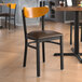 A Lancaster Table & Seating Boomerang Series Black Finish Chair with Dark Brown Vinyl Seat and Cherry Wood Back on a table in a restaurant.