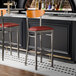 Two Lancaster Table & Seating bar stools with a cherry wood back and burgundy vinyl seats at a bar counter.