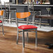 A metal chair with a red vinyl seat and a cherry wood backrest.