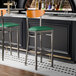 Two Lancaster Table & Seating bar stools with green vinyl seats and cherry wood backs at a black counter.
