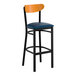 A bar stool with a black metal frame, navy vinyl seat, and a cherry wood curved backrest.