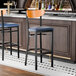A black bar stool with a navy vinyl seat and a cherry wood backrest.
