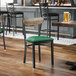 A black metal chair with a green vinyl seat and a driftwood-finished wooden backrest.