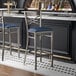 A metal bar stool with a cross back design and a navy blue vinyl padded seat.
