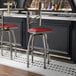 A metal bar stool with a cross back design and a burgundy vinyl padded seat.