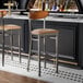 Two Lancaster Table & Seating bar stools with wood backs and light brown vinyl seats at a bar counter.