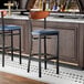 A bar stool with a black metal frame, navy vinyl seat, and an antique walnut wood backrest.
