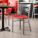 A metal chair with a cross back design and a red vinyl padded seat.