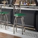 A metal bar stool with a cross back design and a green vinyl padded seat.