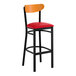 A bar stool with a black metal frame, red vinyl seat, and a cherry wood backrest.