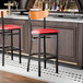 A bar stool with a black metal frame, red vinyl seat, and cherry wood backrest.