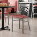 A metal chair with a cross back design and a burgundy vinyl padded seat.