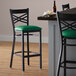 A Lancaster Table & Seating black cross back bar stool with green vinyl padded seat.