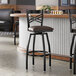 A black metal bar stool with a cross back design and a dark brown vinyl padded seat.