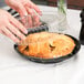 A person putting a clear plastic lid on a pie in a black plastic container.