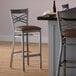 A Lancaster Table & Seating clear coat finish cross back bar stool with a dark brown vinyl padded seat.