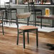 A black metal chair with a light brown vinyl seat and a driftwood-finished wooden backrest.