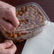 A hand opening a Dart plastic container of almonds.