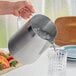 A person pouring water into a stainless steel pitcher.