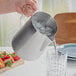 A person pouring ice into an Acopa stainless steel pitcher.