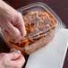 A hand holding a Dart ClearPac plastic container of nuts on a counter.