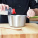 A hand pouring liquid into a Vollrath stainless steel sauce pan.