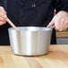 A person stirring a Vollrath stainless steel sauce pan with a wooden spoon.