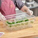 A man in a chef's uniform holding a Cambro clear polycarbonate food pan with broccoli inside.