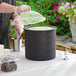 A man using a Carlisle black Coldmaster container with a lid to pour green food into it.